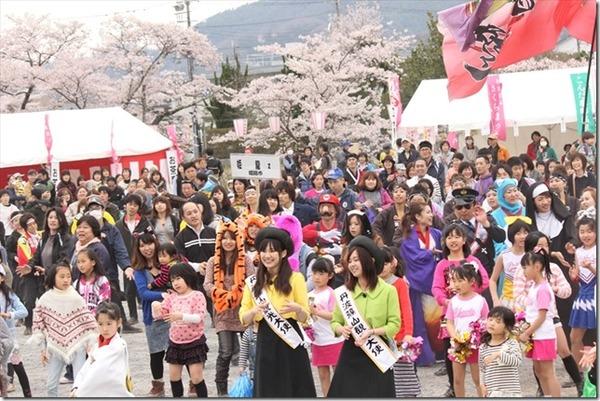 桜が咲いているさくらまつりで観光大使の女性2名を真ん中に人々が踊っている写真